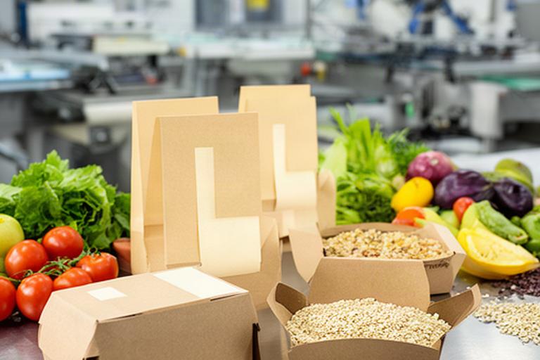 Bedruckte Lebensmittelverpackungen aus Karton neben frischen Produkten in einem Produktionsbetrieb